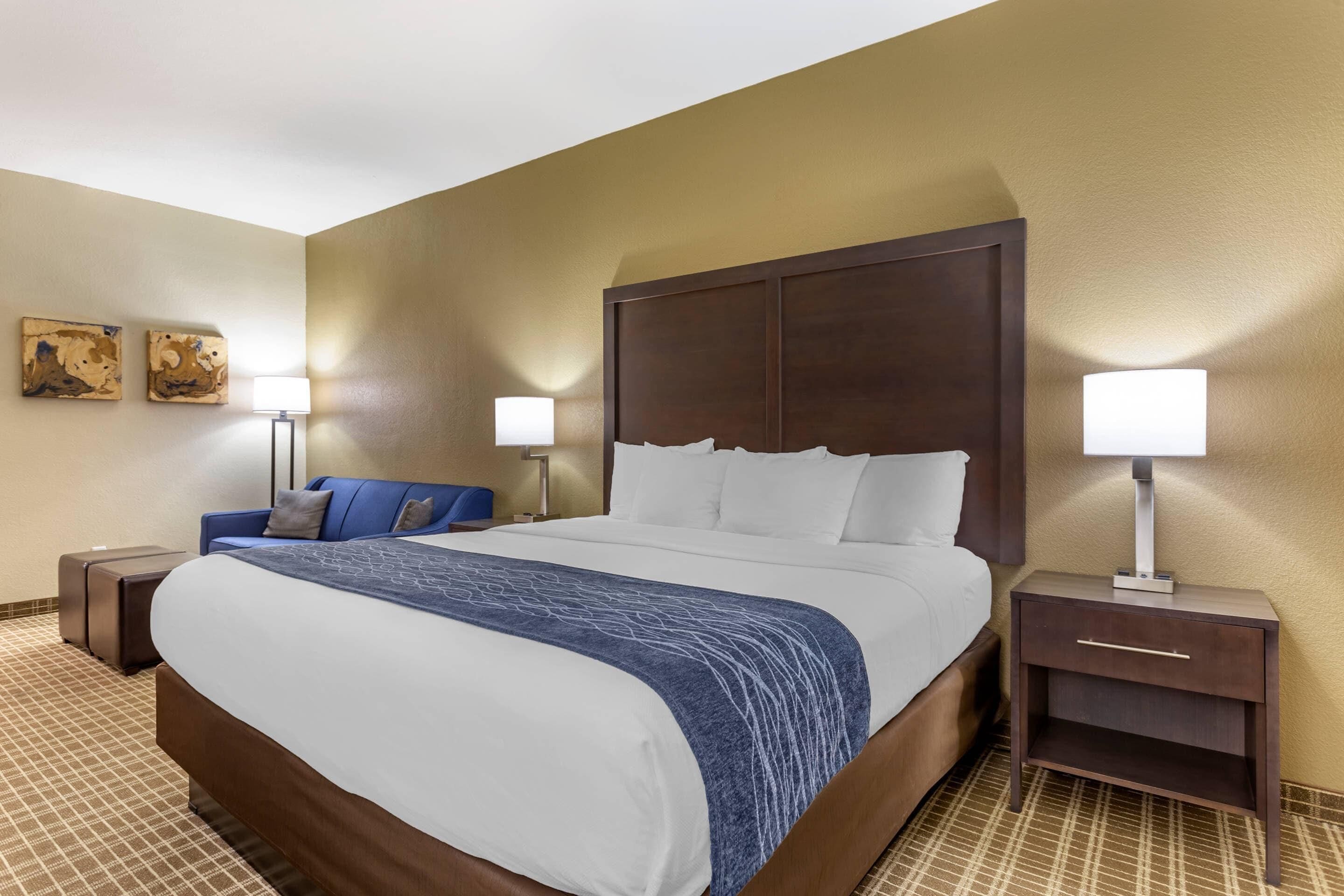 A hotel room with a large bed, two bedside tables, a blue chair, and two wall-mounted lamps.