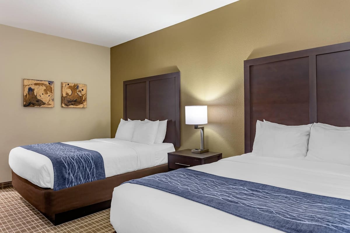 A hotel room with two beds, a nightstand with a lamp, and two abstract paintings on the wall.