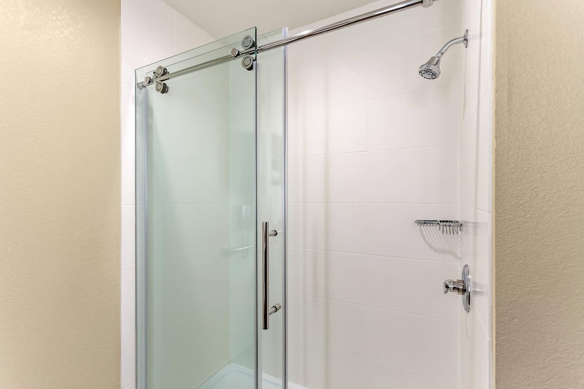 A glass-enclosed shower stall with a handheld showerhead and a wall-mounted faucet.