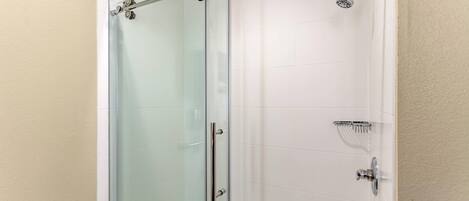 Cabina de ducha con paredes de vidrio, cabezal de ducha de mano y grifo instalado en la pared.