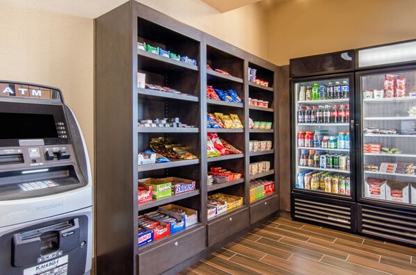 A self-service kiosk with a cash dispenser and a card reader, adjacent to a snack and beverage vending machine.