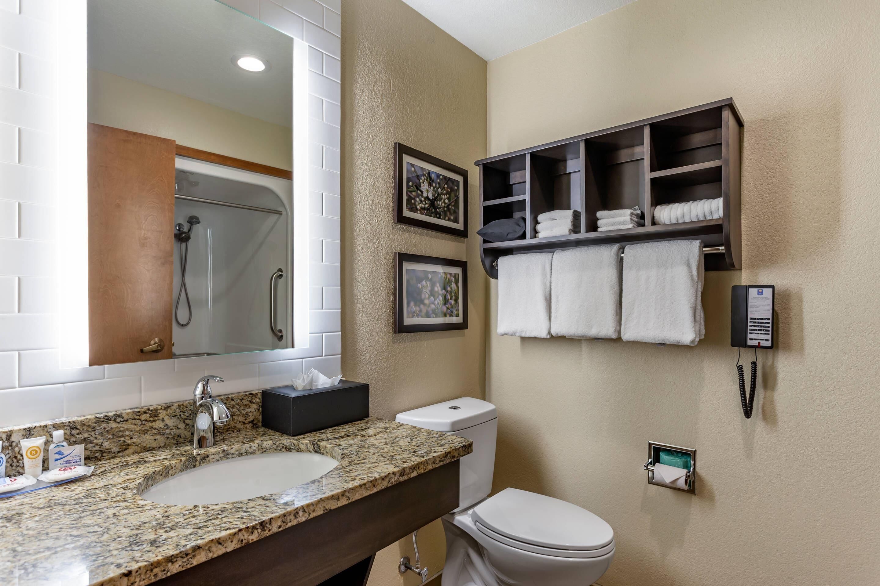 A bathroom with a granite sink, a white toilet, a shower, and a towel rack with towels.