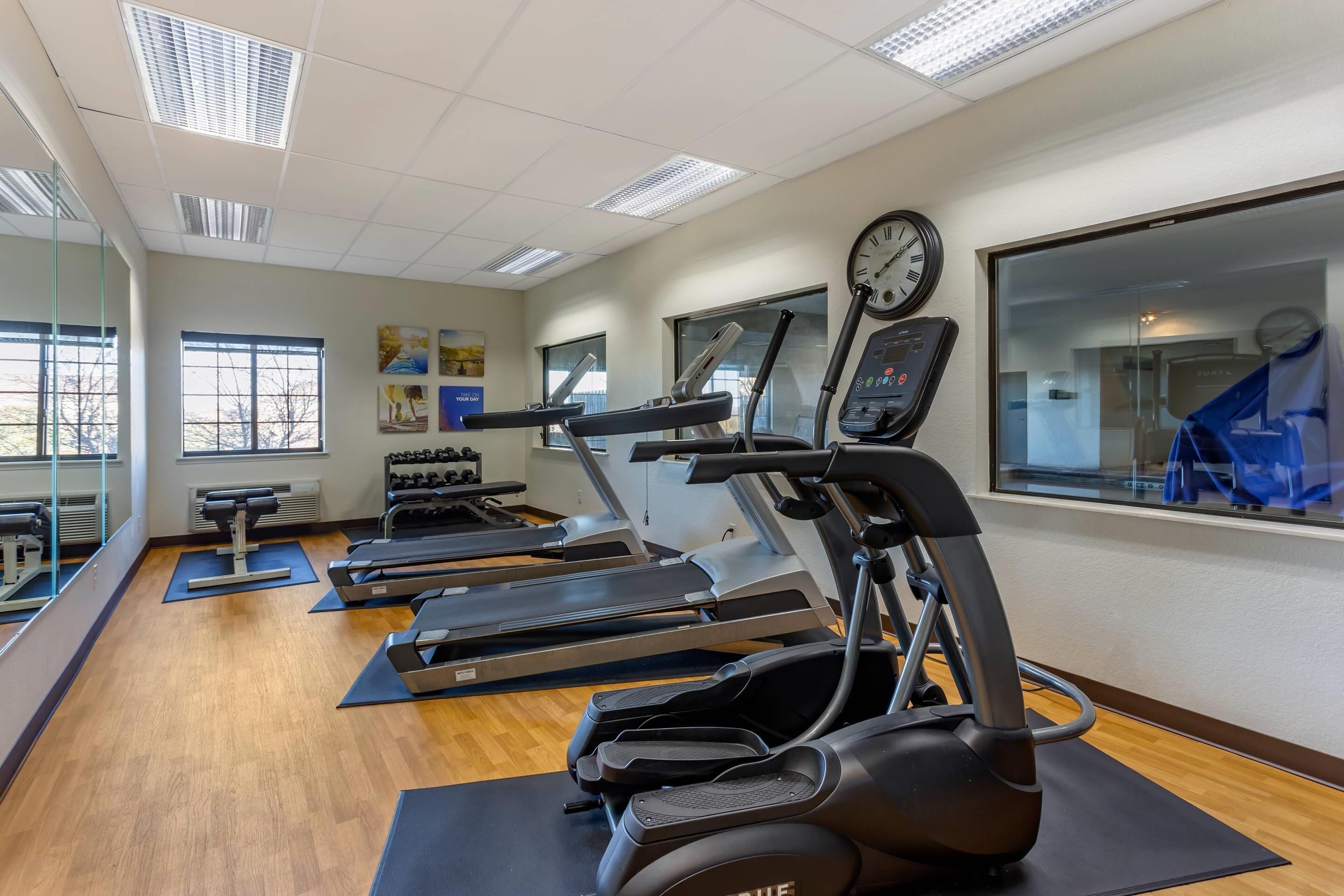 Une salle de sport équipée de tapis de course, de vélos elliptiques et d’une horloge au mur.
