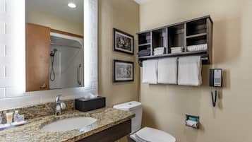 Un baño con lavamanos de encimera de granito, inodoro, ducha y toallero.