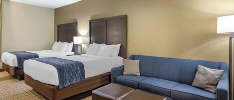 A hotel room with two beds, a sofa, and a small table.