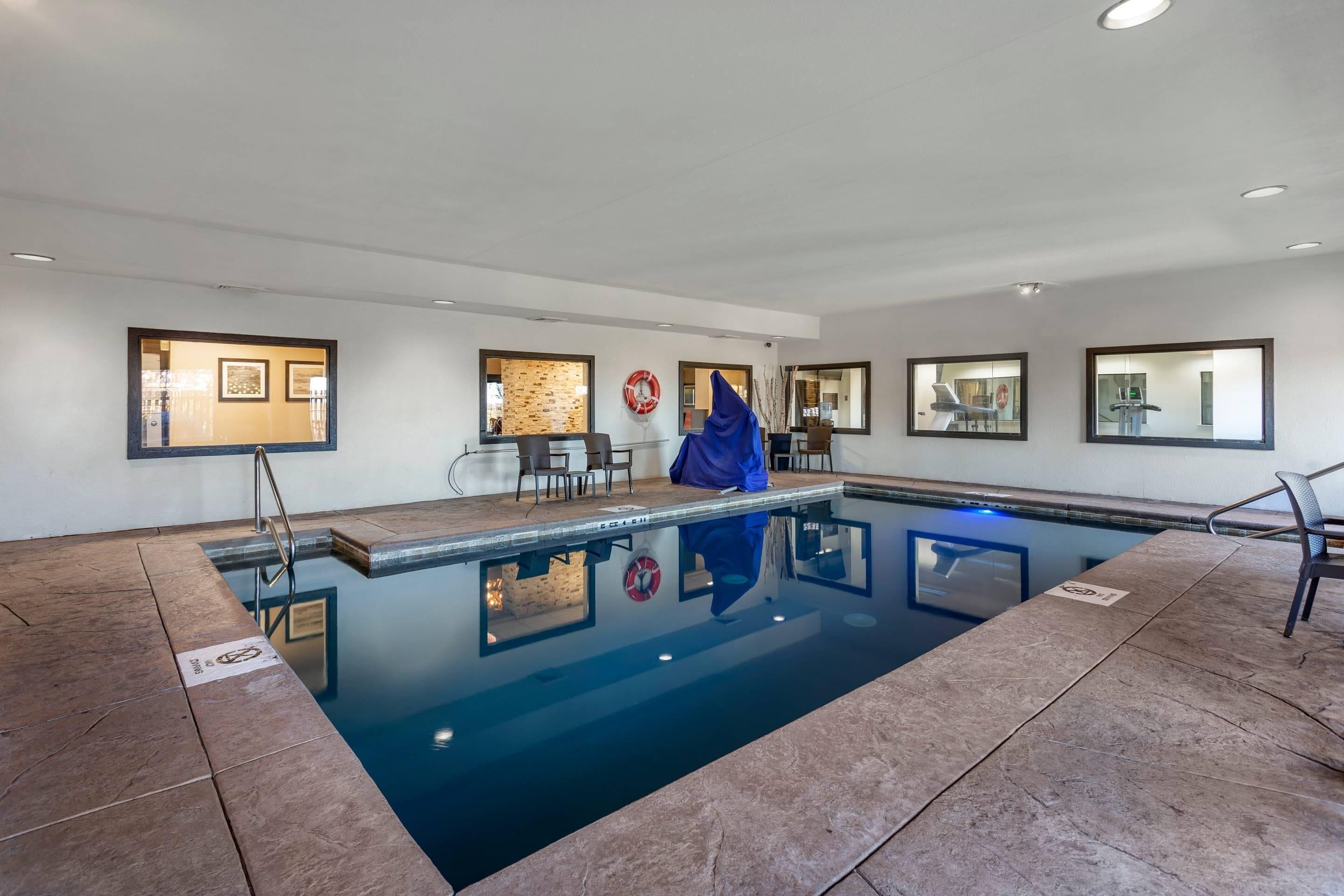 Una piscina interior moderna con agua cristalina, una zona de descanso con sillones y un suelo de baldosas de piedra.