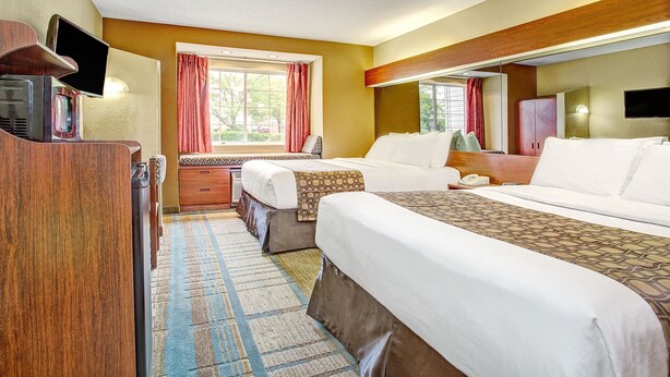 A hotel room with two beds, a TV, a desk, and a window with curtains. - Microtel Inn & Suites by Wyndham Mason/Kings Island (Mason)