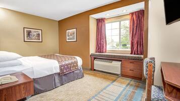 Une chambre d’hôtel avec un lit, un bureau, une chaise, une fenêtre avec des rideaux et deux tableaux encadrés au mur.