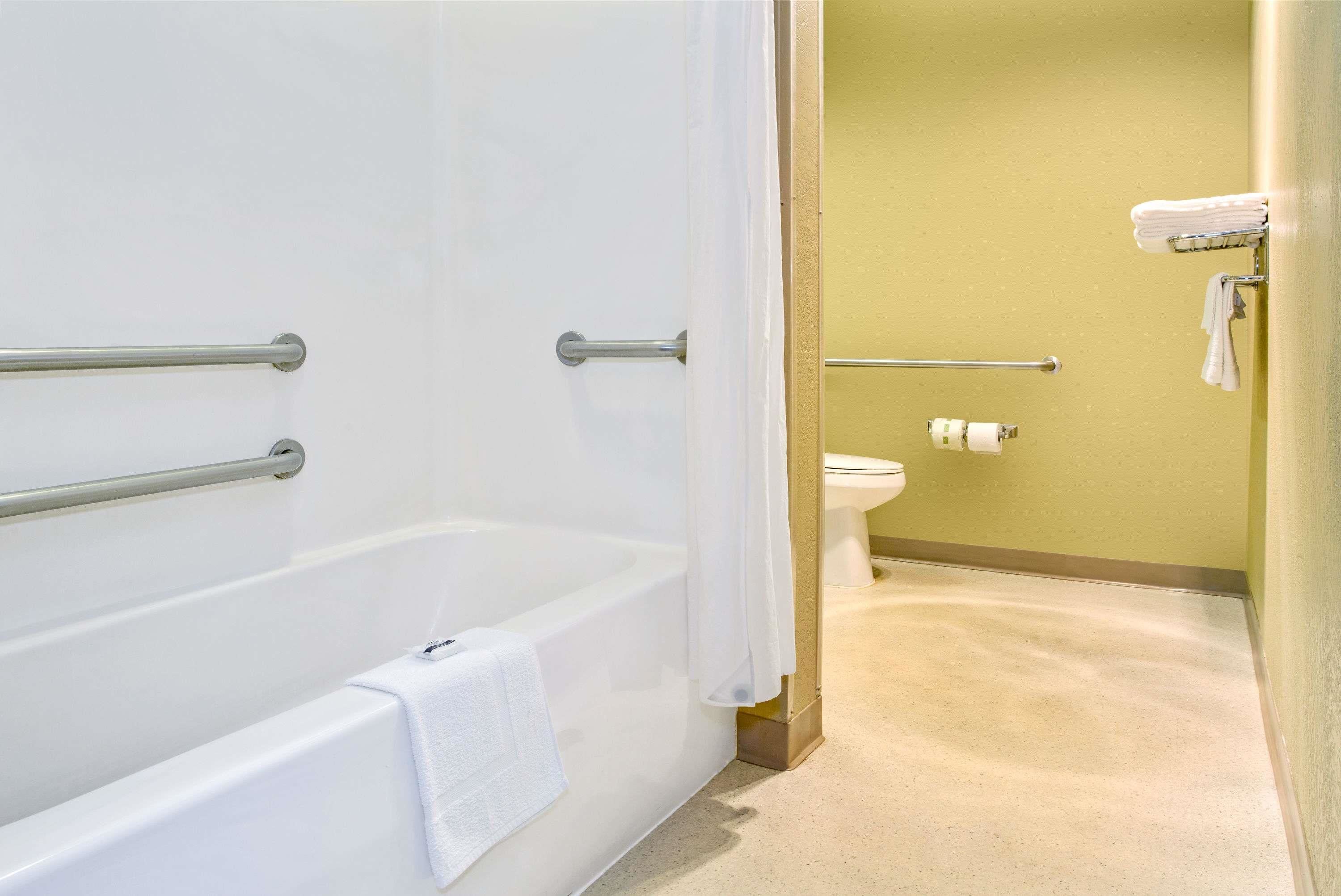 A bathroom with a bathtub, grab bars, a toilet, and a towel rack.