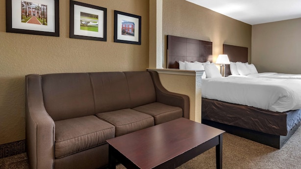 Een hotelkamer met een bruine bank, een houten bijzettafeltje, een bed met witte lakens en drie ingelijste foto's aan de muur.