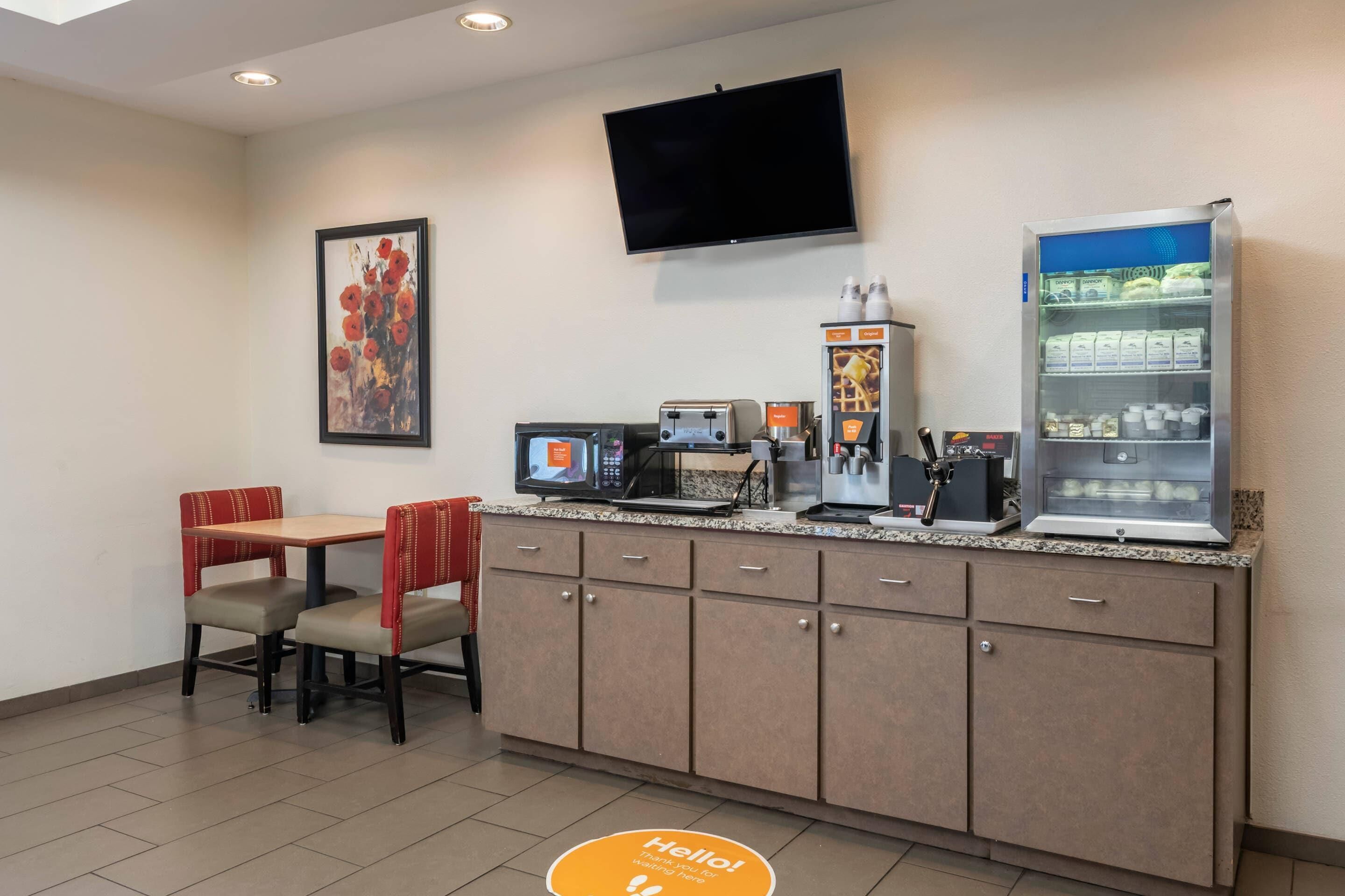 A hotel lobby with a seating area, a coffee machine, a television, and a refrigerator.