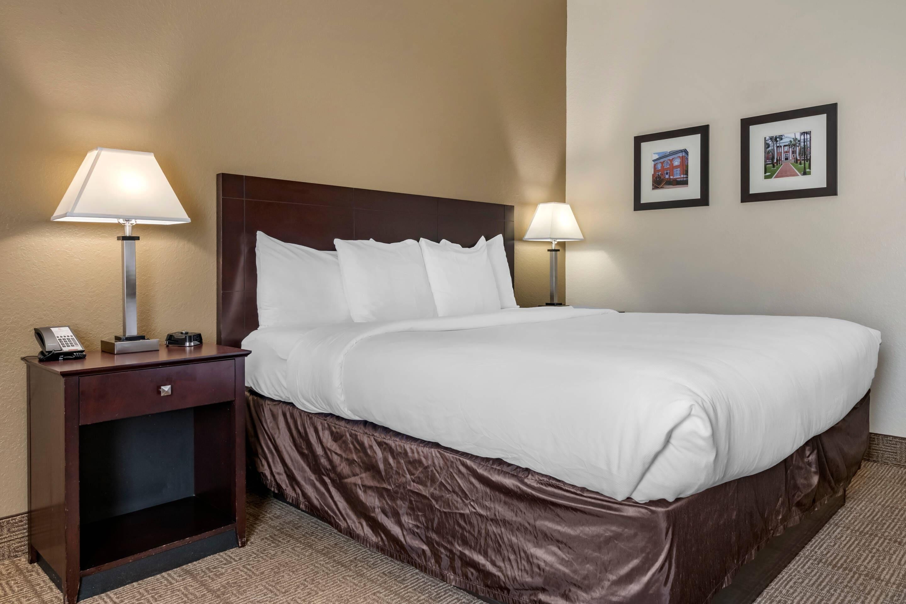 A hotel room with a large bed, two bedside lamps, a nightstand with a phone, and two framed pictures on the wall.