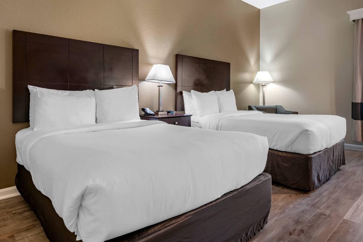 A hotel room with two beds, each with white linens, a dark headboard, bedside lamps, and a wooden floor.