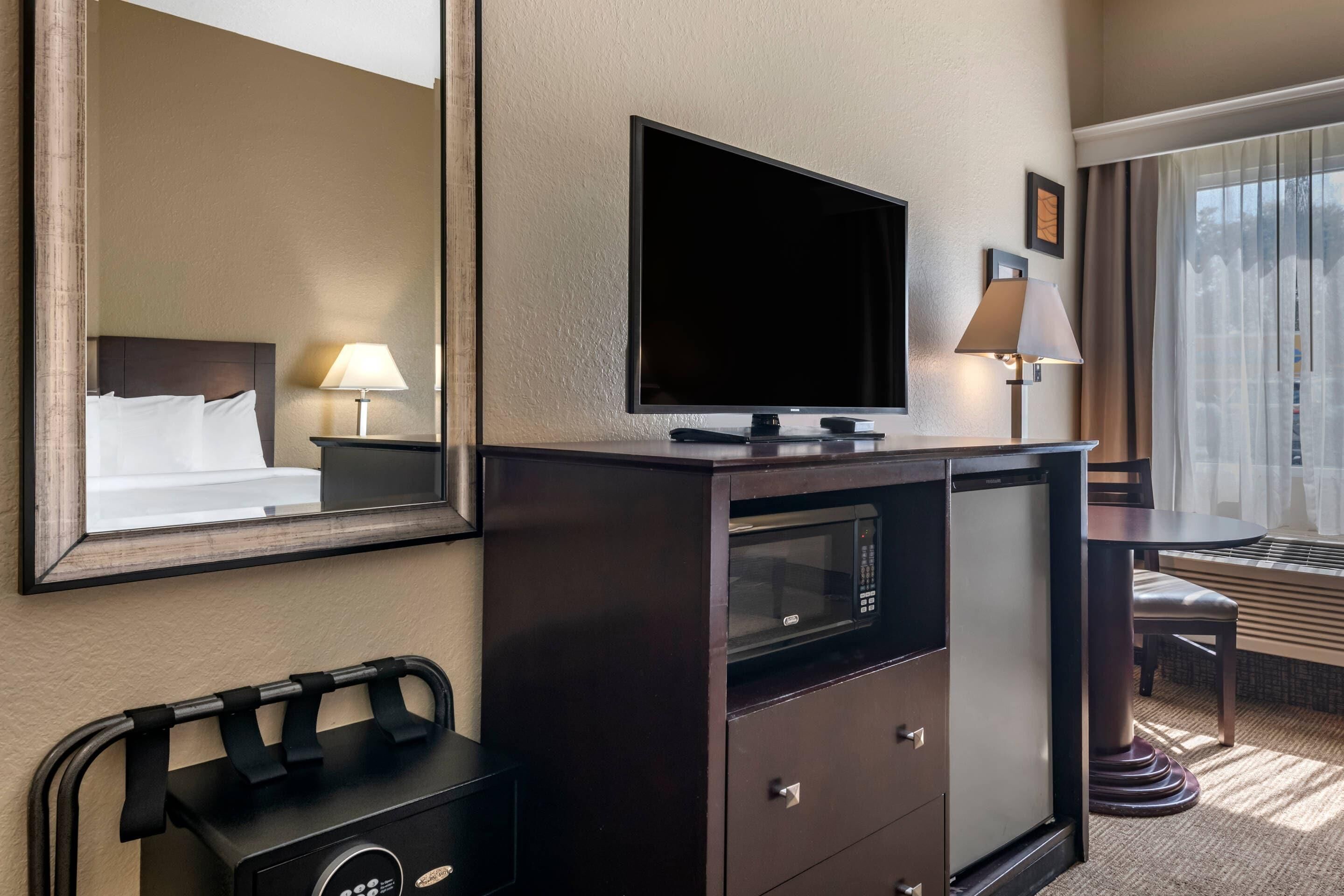 A hotel room with a large bed, a flat-screen TV, a minibar, a desk with a lamp, and a window with curtains.