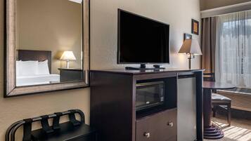 A hotel room with a large bed, a flat-screen TV, a minibar, a desk with a lamp, and a window with curtains.