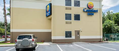 A Comfort Inn hotel with a beige and white exterior, a parking lot, and a palm tree in the foreground.