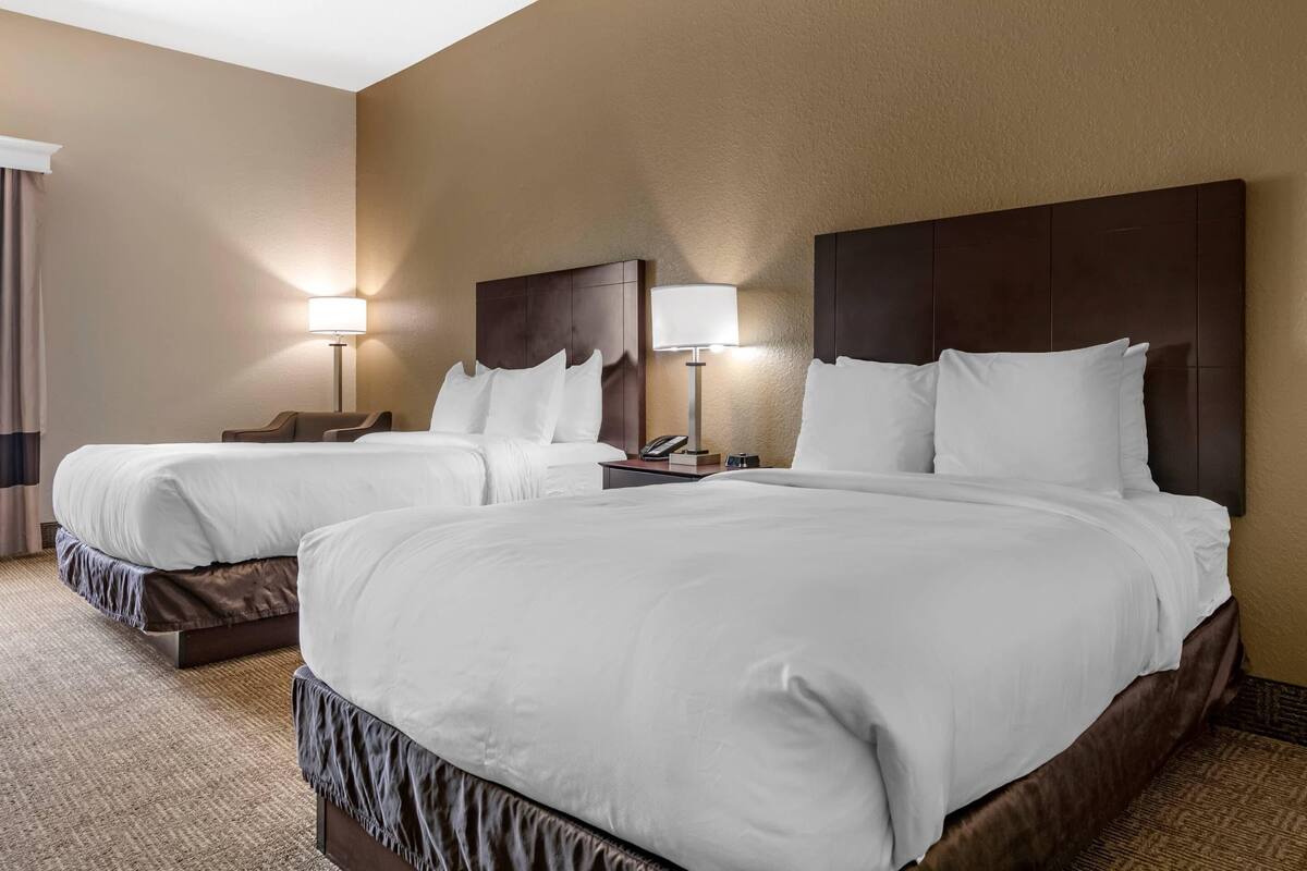 A hotel room with two beds, a nightstand, a lamp, and a wall-mounted mirror.