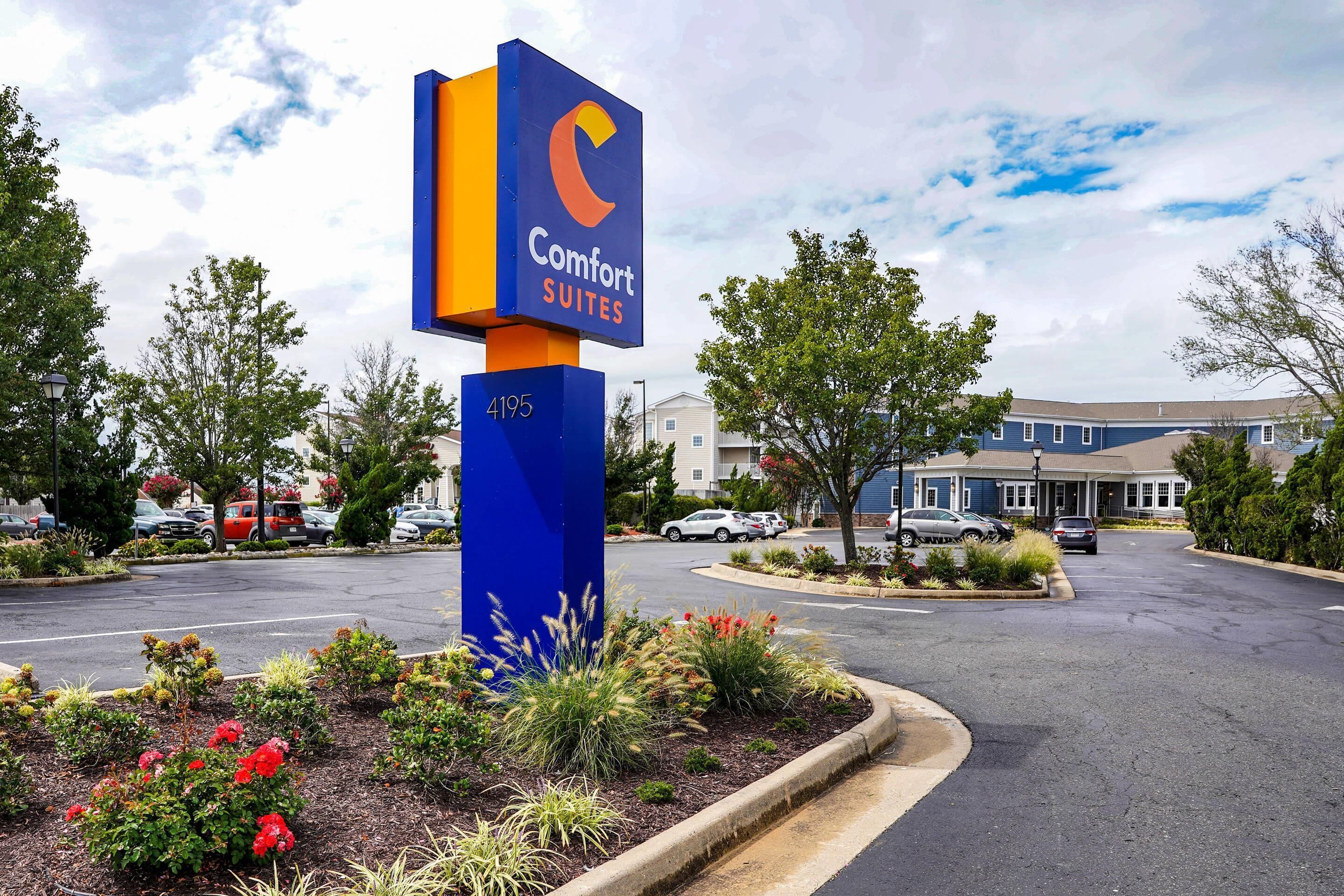A Comfort Suites hotel sign with a blue and orange color scheme, surrounded by landscaped gardens and a parking lot.