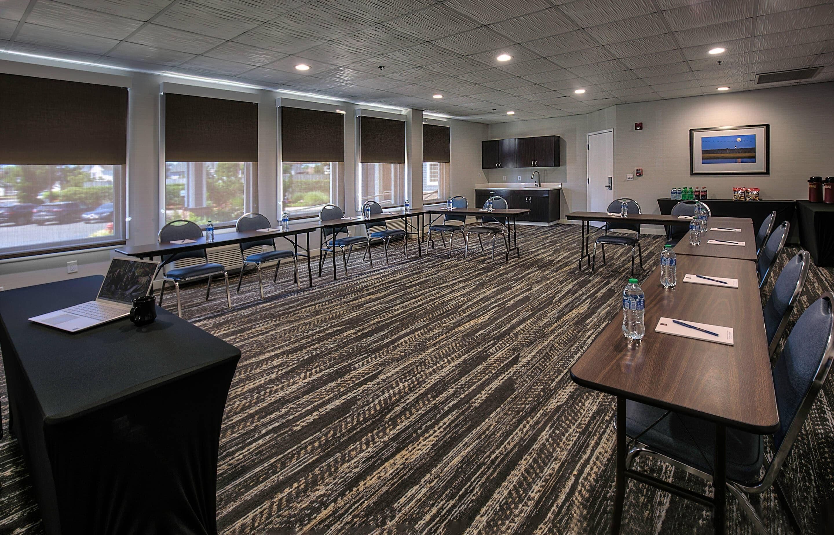 A conference room with a long table, chairs, a laptop, and a projector screen.