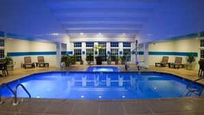 An indoor swimming pool with clear water, surrounded by lounge chairs and potted plants.