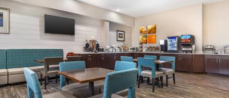A hotel lobby with a seating area, a counter with a coffee machine, and a television mounted on the wall.