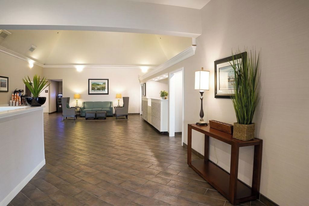A spacious hallway with a reception desk, a seating area with a sofa and chairs, and a console table with a lamp and plant.