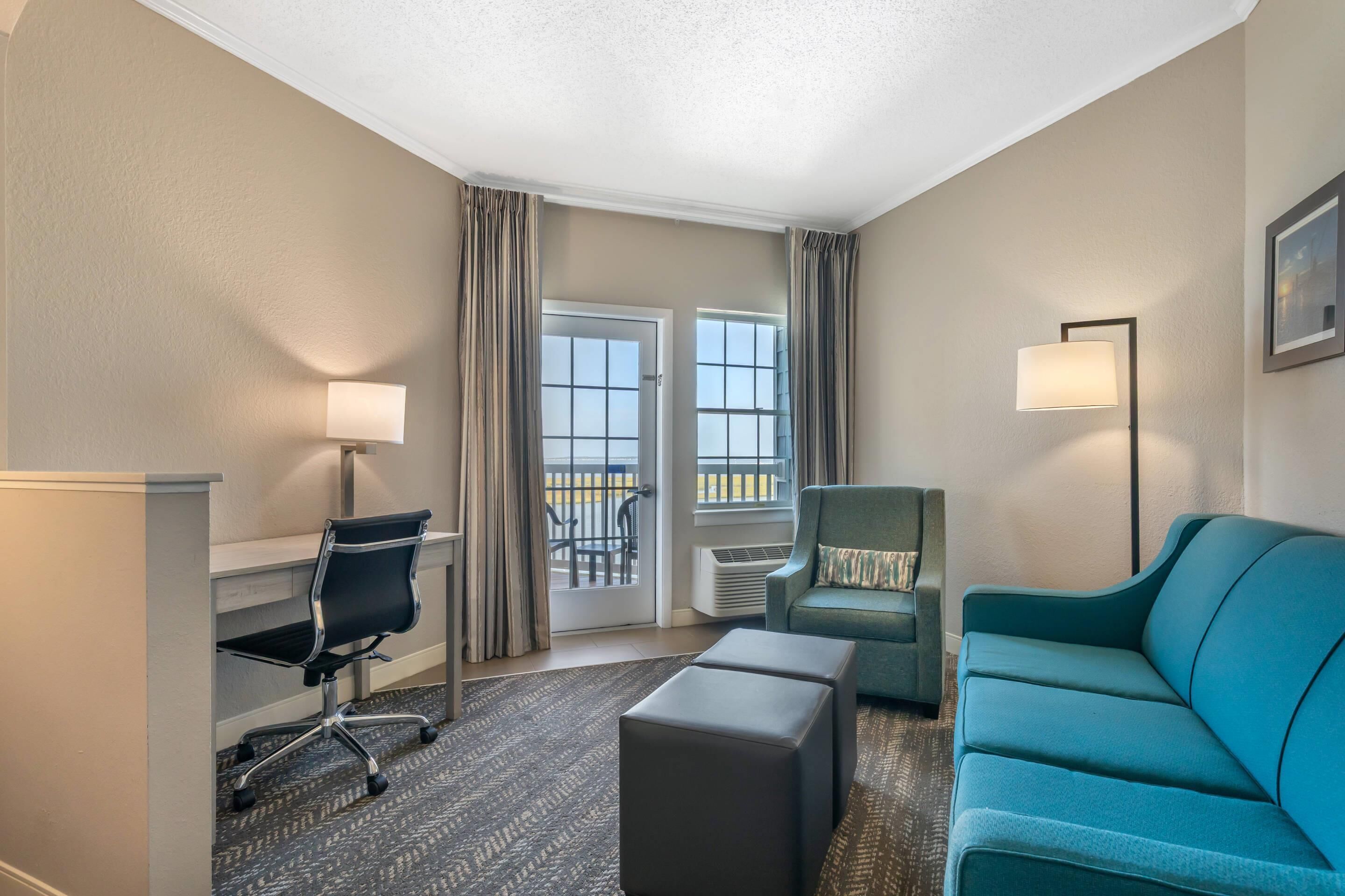 Habitación de hotel con escritorio, silla, sofá y vistas al exterior mediante una puerta corredera.