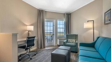 Habitación de hotel con escritorio, silla, sofá y vistas al exterior mediante una puerta corredera.