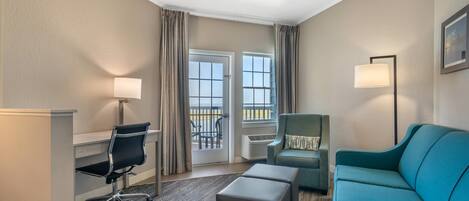 Habitación de hotel con escritorio, silla, sofá y vistas al exterior mediante una puerta corredera.