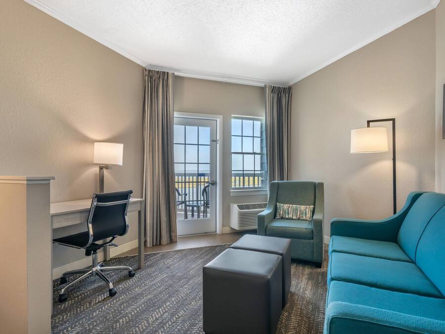 Habitación de hotel con escritorio, silla, sofá y vistas al exterior mediante una puerta corredera.