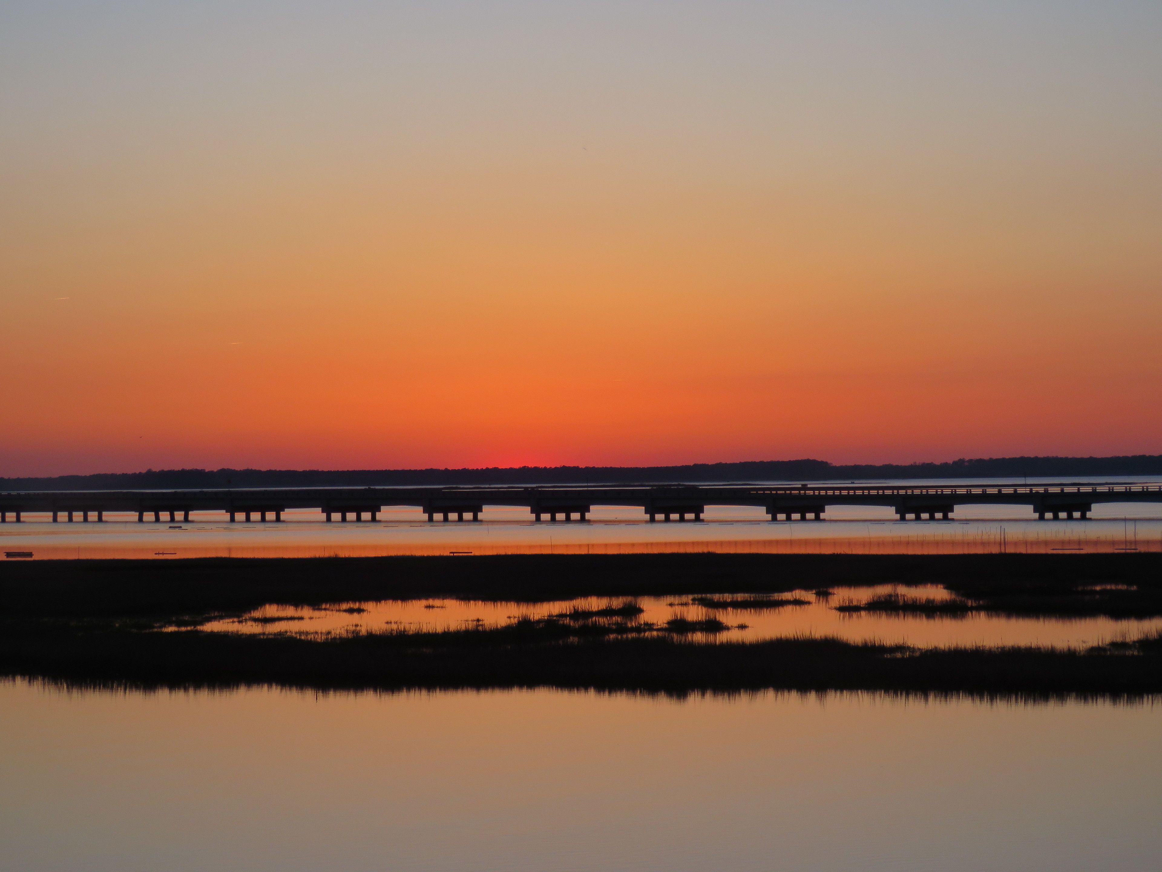 Un atardecer sobre una masa de agua tranquila con un puente que la atraviesa.