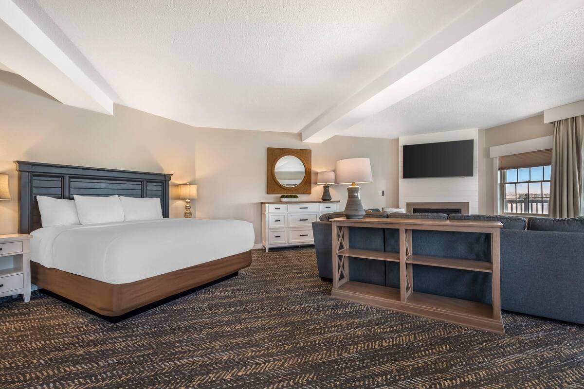 A hotel room with a large bed, a desk, a sofa, a TV, and a window with curtains.
