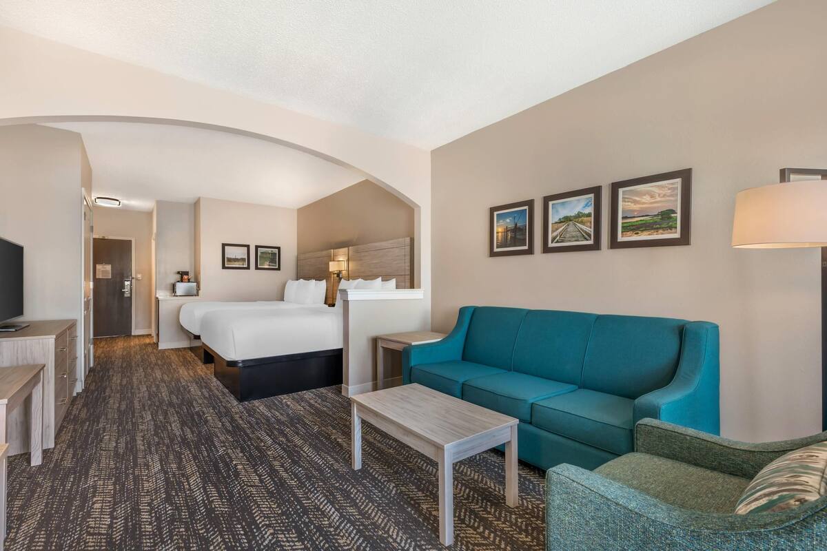 A hotel room with a bed, a teal sofa, a small table, and a TV.