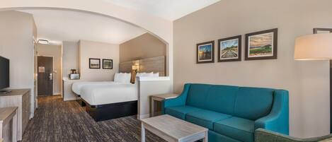 Une chambre d’hôtel avec un lit, un canapé de couleur turquoise, une petite table et un téléviseur.