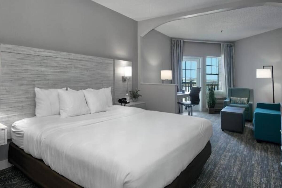 A hotel room with a large bed, bedside tables, a desk, a chair, and a view of the outside.