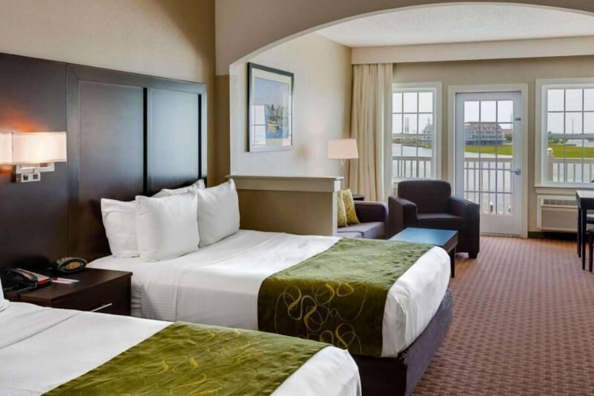 A hotel room with two beds, a desk, a chair, and a view of the outside.