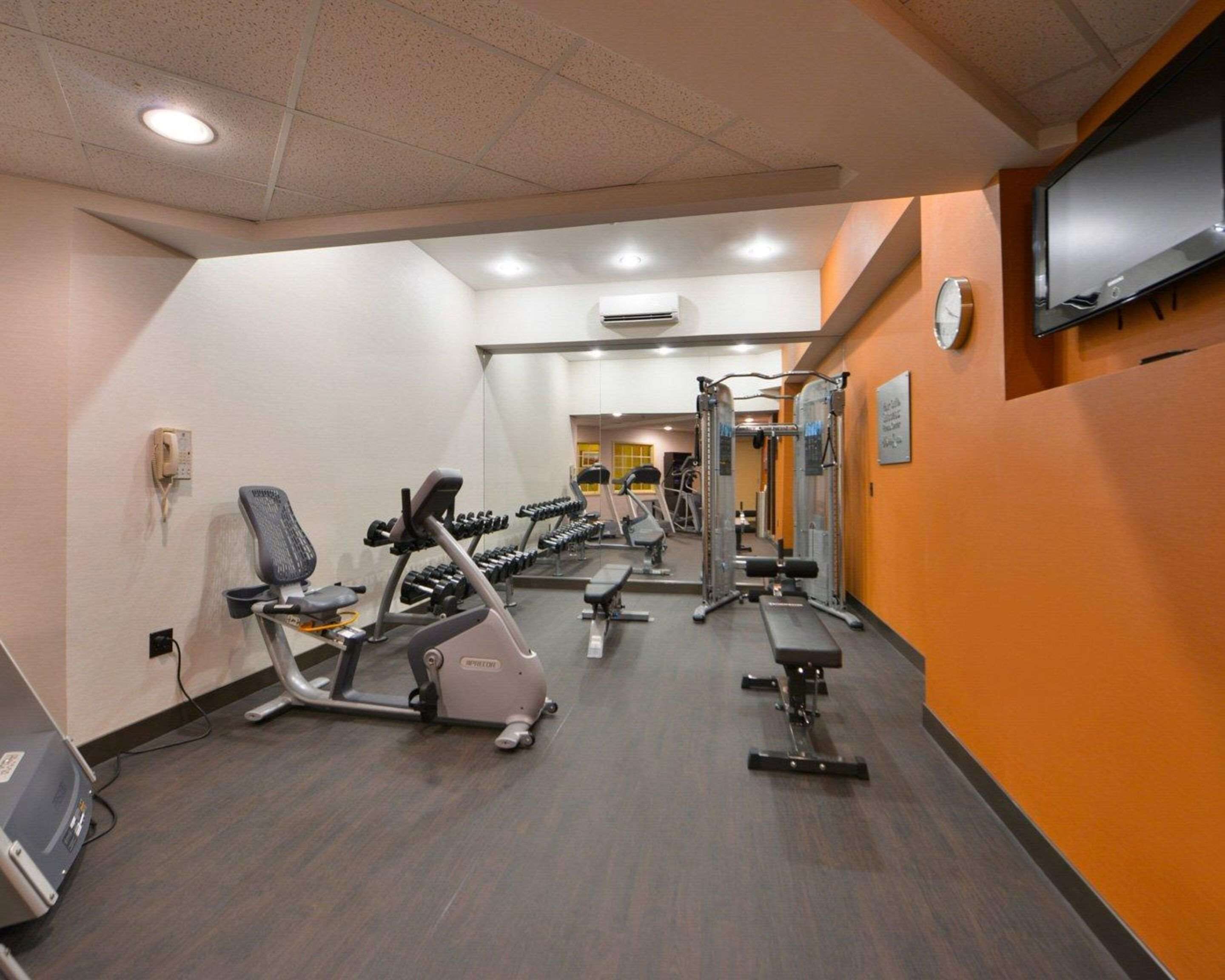 A gym with cardio equipment, weight machines, and a television on the wall.