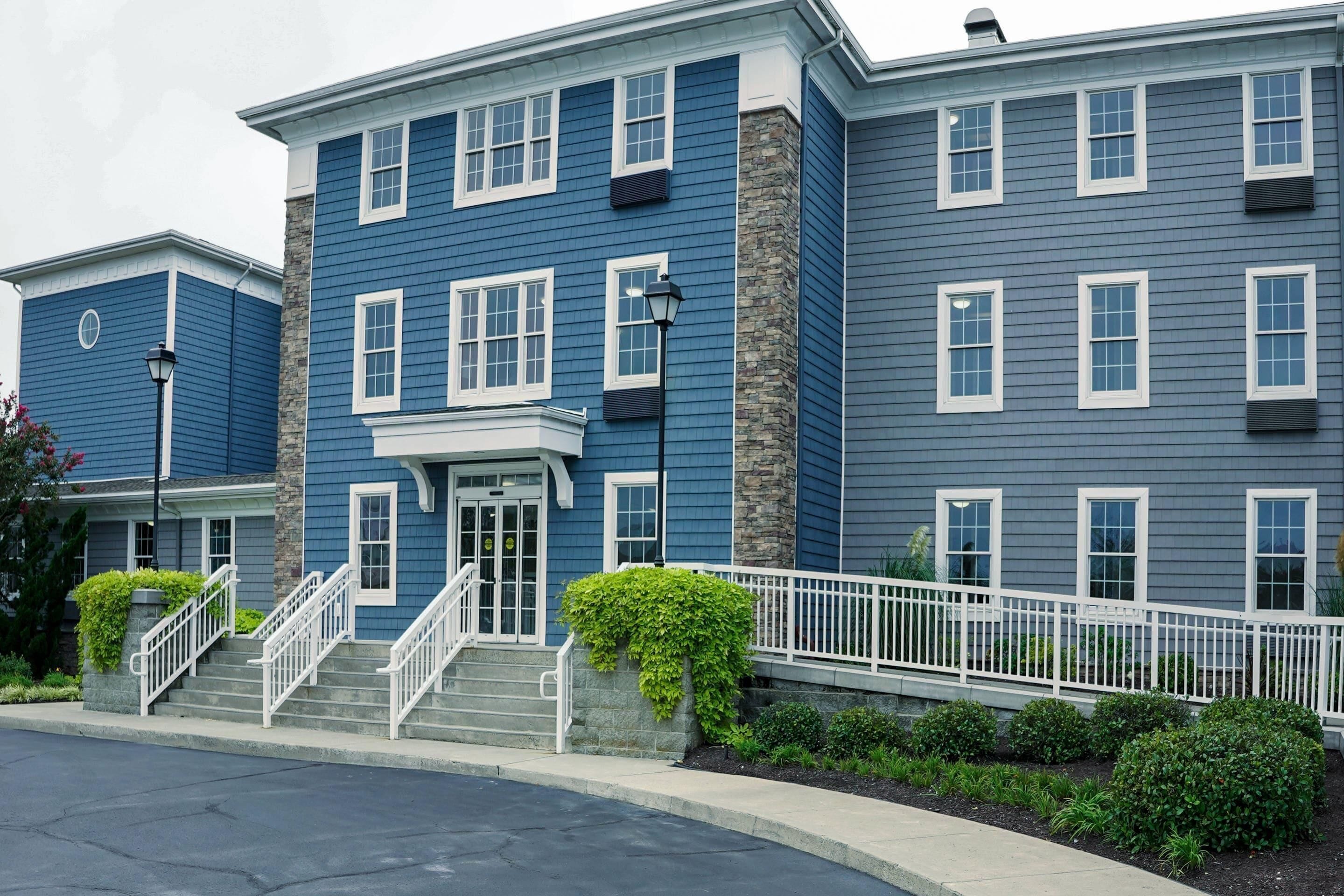 A multi-story residential building with a central entrance, a staircase, and a white fence.