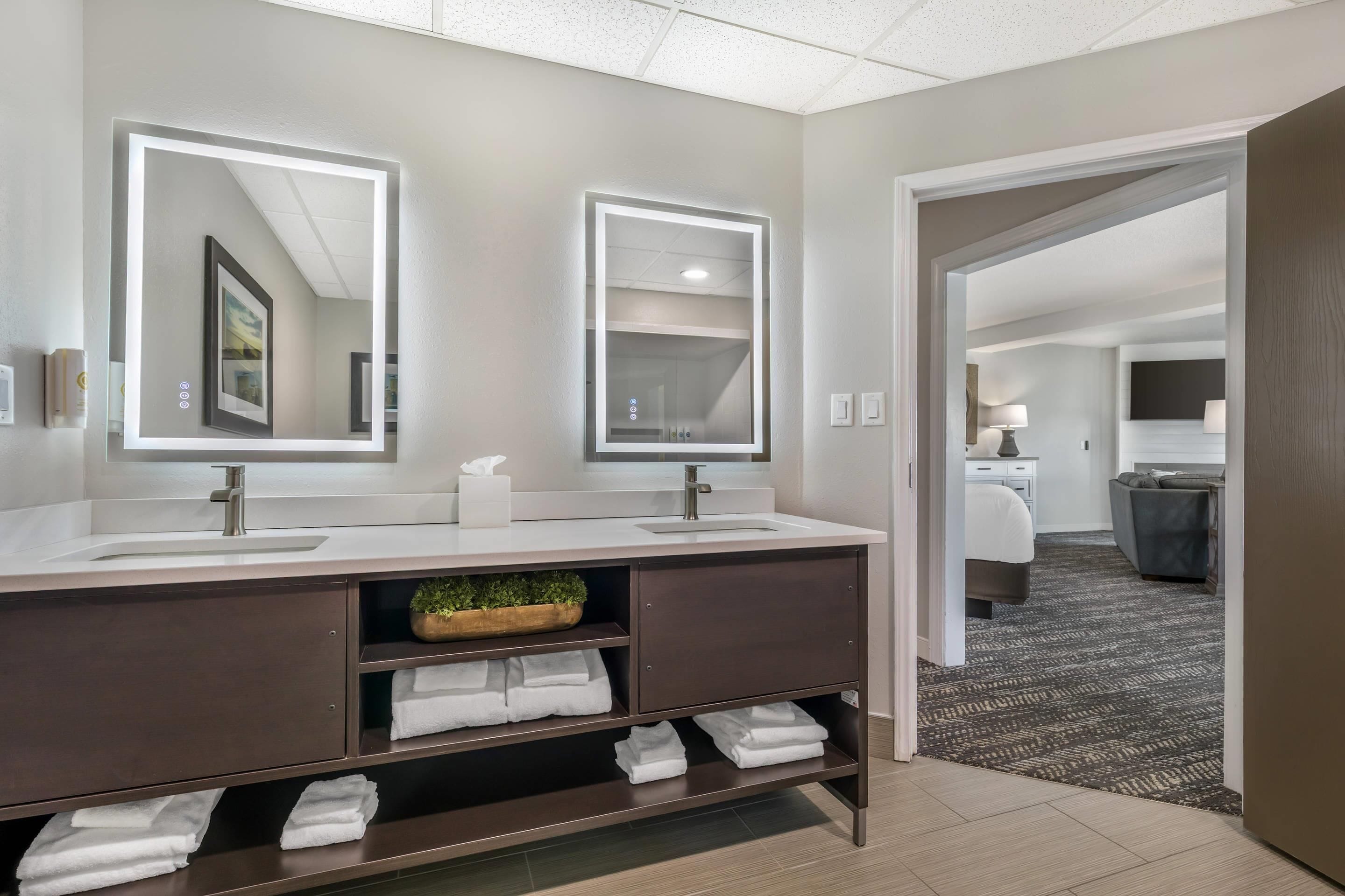Un baño moderno con lavamanos dobles, un espejo grande y un mueble de tocador con espacio para toallas.
