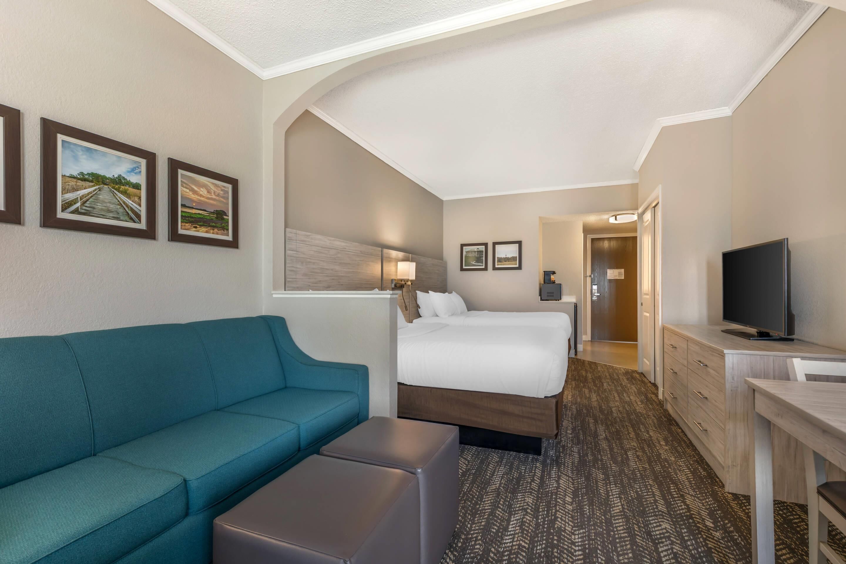 A hotel room with a bed, a sofa, a desk, and a television.