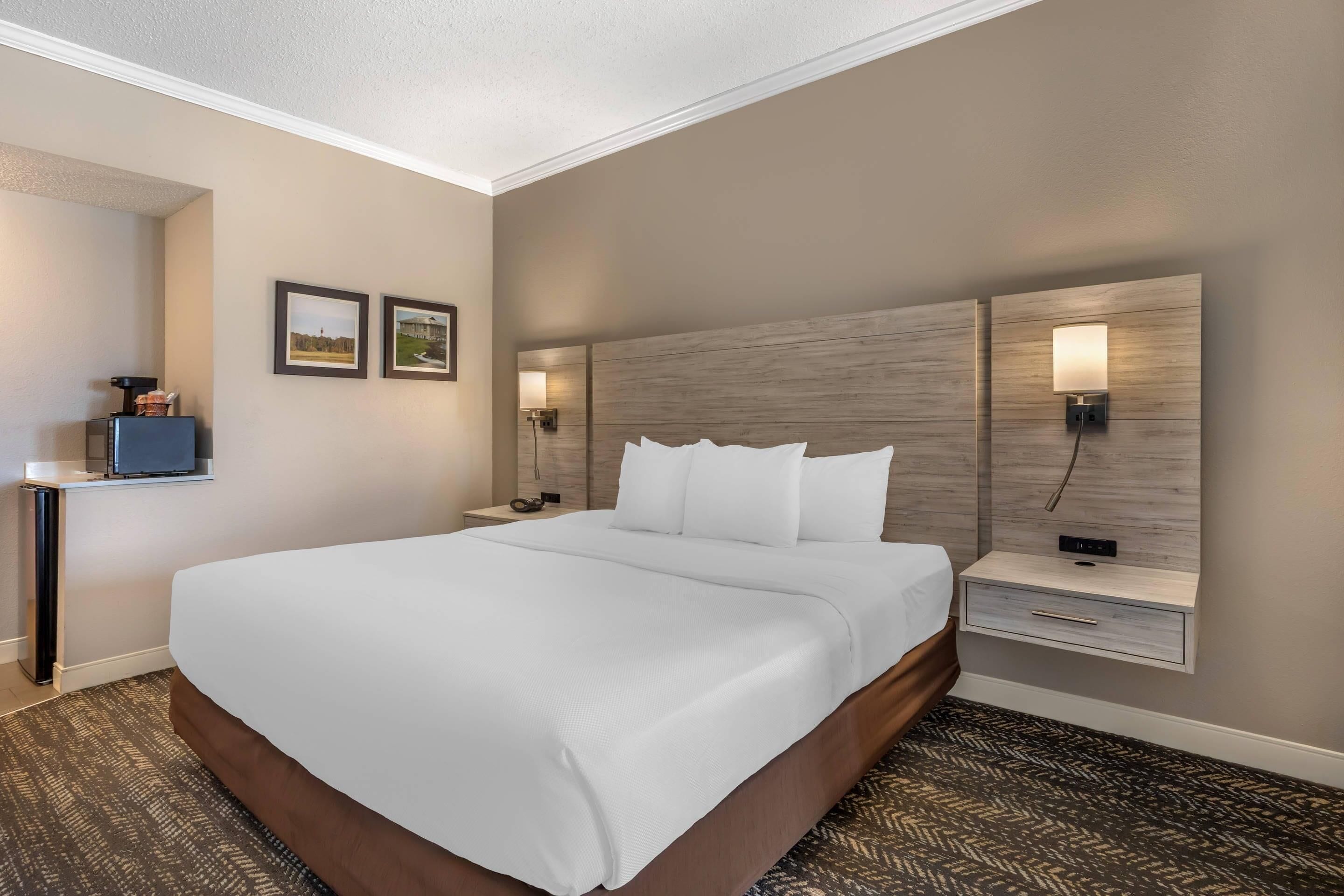 A hotel room with a large bed, two bedside tables with lamps, a small desk with a chair, and framed pictures on the wall.