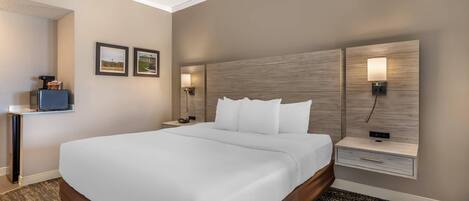 A hotel room with a large bed, two bedside tables with lamps, a small desk with a chair, and framed pictures on the wall.