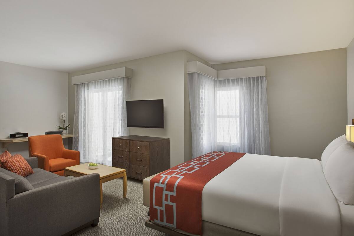 Ein Hotelzimmer mit Bett, Sofa, Fernseher, Schreibtisch und Stuhl.