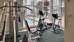 A gym with exercise equipment, large windows, and a view of a pool and buildings. - Corporate Inn Sunnyvale (Sunnyvale)