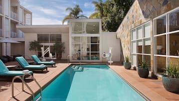 A swimming pool with lounge chairs, a glass-enclosed area, and potted plants.