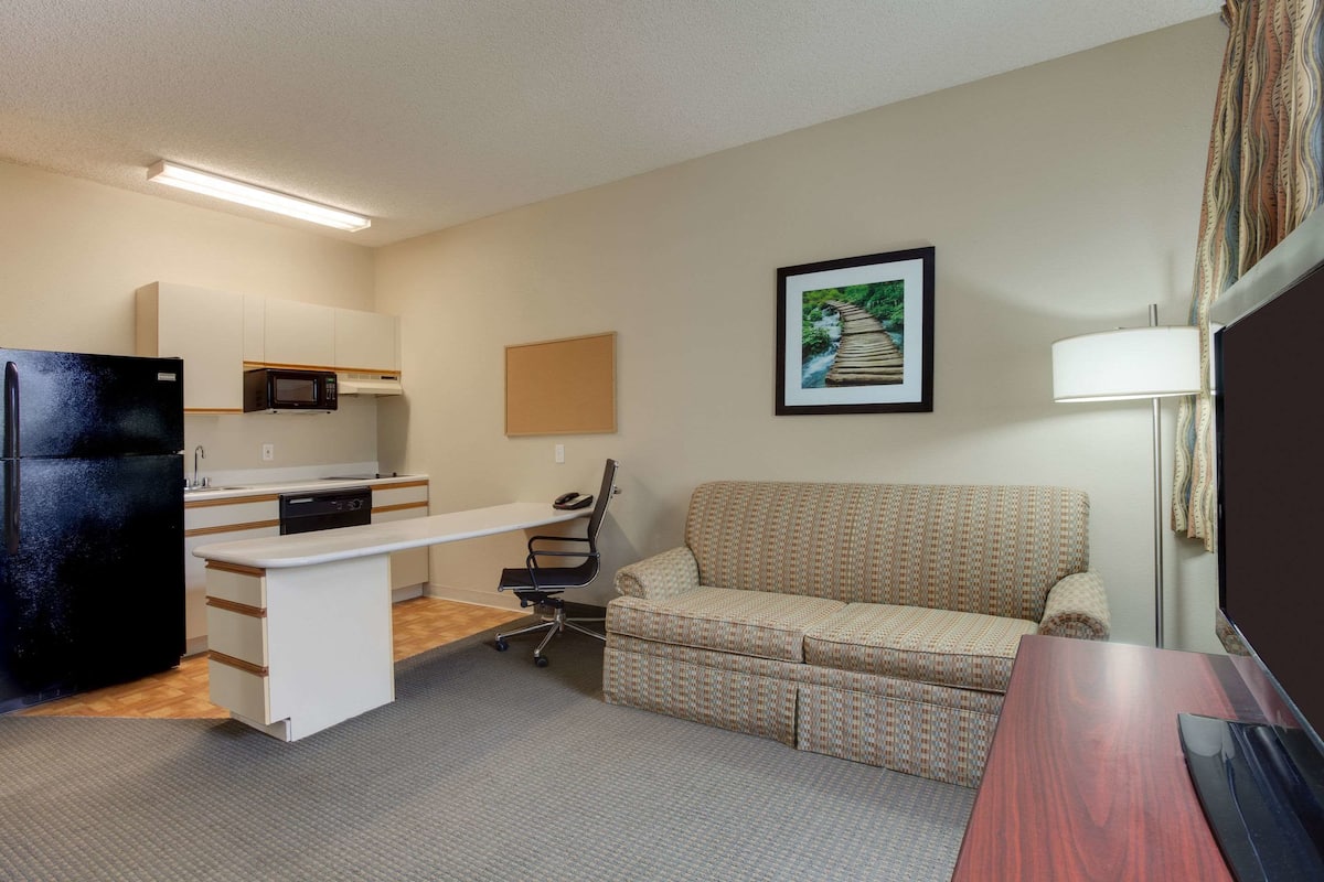 Un espacio habitable pequeño con kitchenette, un sofá, un escritorio y un televisor.