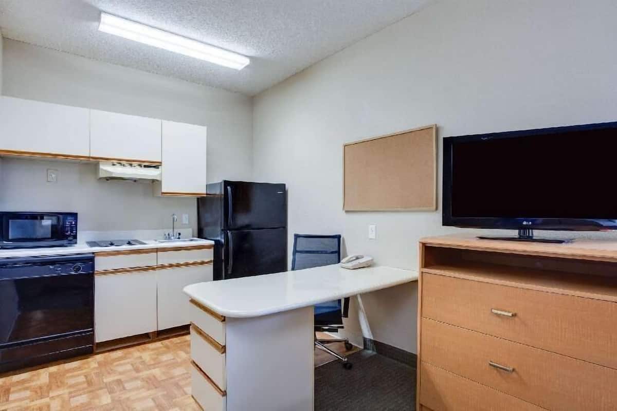 Cocina compacta con microondas, estufa, refrigerador y un televisor grande sobre un mueble de madera.