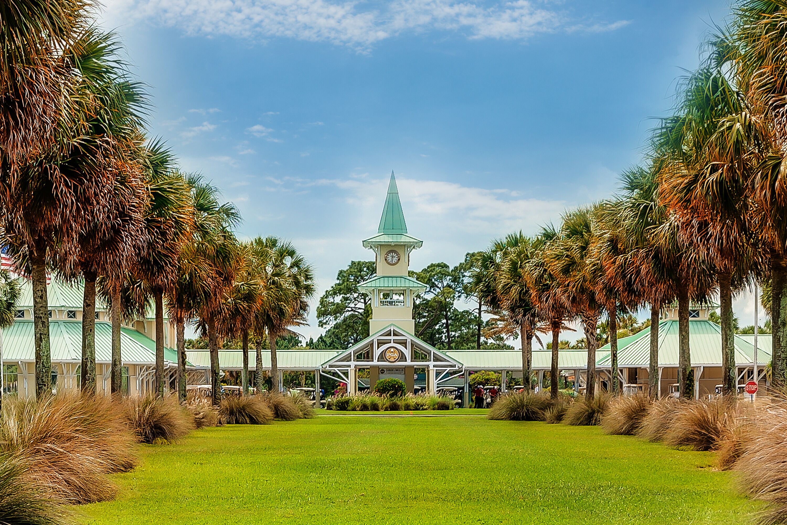 A church with a clock tower, surrounded by palm trees and a well-maintained lawn.