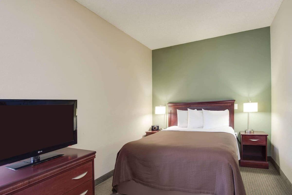 Una habitación de hotel con una cama, un televisor sobre un aparador de madera, dos lámparas de noche y una mesita de noche.