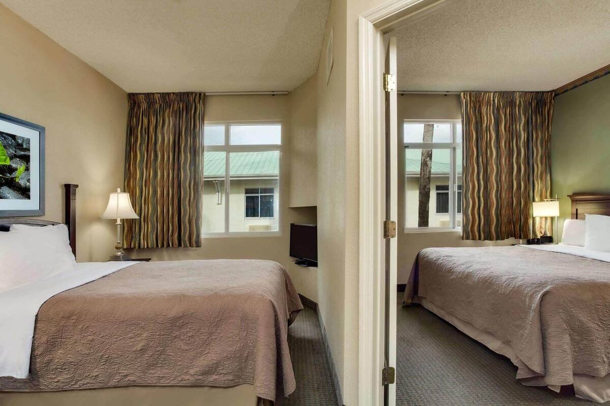 Habitación de hotel con dos camas, televisión, escritorio y ventana con cortinas.